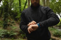 Молодой человек использует умные часы в лесу — стоковое фото