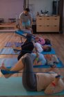 Trainer assisting senior women in performing yoga at yoga center — Stock Photo