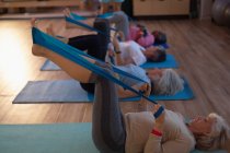 Group of senior women performing yoga with yoga band in yoga center — Stock Photo