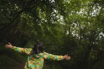 Вид ззаду дівчини з простягнутими руками, стоячи в лісі — стокове фото