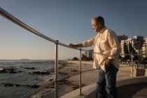 Hombre mayor de pie cerca del mar en el paseo marítimo en un día soleado - foto de stock
