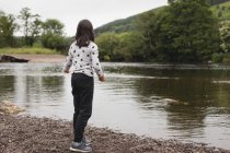 Chica joven de pie cerca de la orilla del río - foto de stock