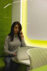 Бізнес-леді розмовляє на мобільному телефоні, використовуючи ноутбук в офісі — стокове фото