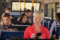Nachdenkliche Pendlerin nutzt Handy während der Fahrt im modernen Bus — Stockfoto