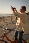 Старший мужчина фотографирует у моря на набережной в солнечный день — стоковое фото