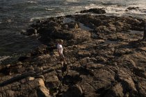 Uomo anziano che cammina sulla roccia in spiaggia nella giornata di sole — Foto stock