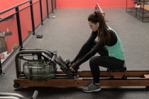 Young woman using rowing machine in fitness studio — Stock Photo