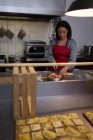 Женщина пекарь резки тесто во время подготовки к макаронных изделий в пекарне — стоковое фото