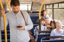 Умный мужчина, пользующийся мобильным телефоном во время поездки в современном автобусе — стоковое фото