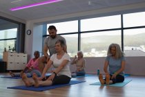 Тренер, помогающий старшим женщинам в йоге в центре йоги — стоковое фото