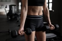 Mid section of women exercising with dumbbell in fitness studio — Stock Photo