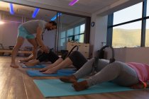 Entrenador asistiendo a mujeres mayores en la realización de yoga en el centro de yoga - foto de stock