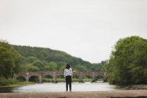 Вид ззаду дівчини, що стоїть на навколишній стіні біля берега річки — стокове фото