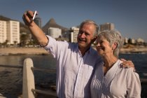 Sonriendo pareja mayor tomando selfies en el paseo marítimo - foto de stock