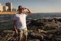Senior steht an sonnigem Tag auf Felsen in der Nähe des Meeres — Stockfoto