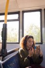 Joven viajera femenina que aplica maquillaje mientras viaja en autobús moderno - foto de stock