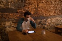 Мужчина пьет кофе во время использования цифровой вкладки — стоковое фото