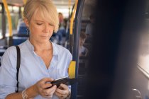 Жінка-комісарка використовує мобільний телефон під час подорожі в сучасному автобусі — стокове фото