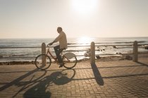 Старший чоловік їде на велосипеді на набережній в сонячний день — стокове фото