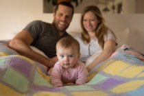 Los padres con el bebé acostado en la cama en el dormitorio en casa - foto de stock
