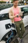 Человек с цифровым планшетом во время зарядки электромобиля на зарядной станции — стоковое фото