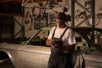 Мужской механик с помощью мобильного телефона в гараже — стоковое фото