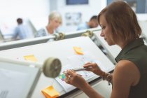 Female executive working on drafting table in office — Stock Photo