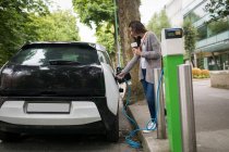 Молодая женщина заряжает электромобиль на зарядной станции — стоковое фото