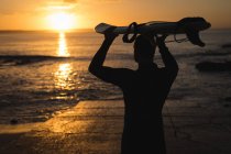 Surfista carregando a prancha na cabeça na praia — Fotografia de Stock