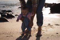 Close-up of father teaching baby to walk at beach — Stock Photo