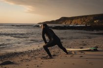 Surfer stretching on beach during sunset — Stock Photo
