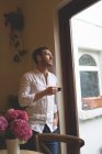 Удумливий чоловік має каву, стоячи біля вікна вдома — стокове фото
