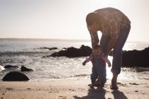 Padre enseñando al bebé a caminar en la playa en un día soleado - foto de stock