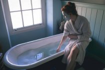 Женщина сидит на ванне, проверяя воду в ванной комнате дома — стоковое фото