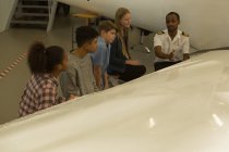 Pilota maschio che spiega di aeroplano ai bambini in istituto di formazione — Foto stock