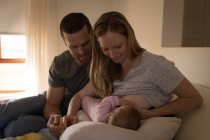 Mother breastfeeding to baby while father sitting beside her on bed at home — Stock Photo