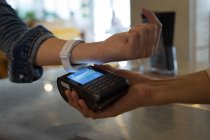 Крупный план женщины, платящей с помощью технологии NFC на смарт-часах в кафе — стоковое фото