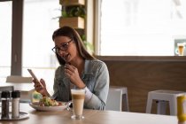 Mulher usando telefone celular enquanto tem comida no café — Fotografia de Stock