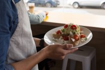Primer plano del camarero sosteniendo el plato de comida en la cafetería - foto de stock