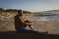 Pensativo hombre sentado en el paseo marítimo cerca de la playa - foto de stock