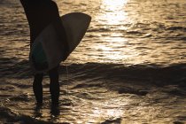 Low section of surfer with surfboard standing on beach — Stock Photo
