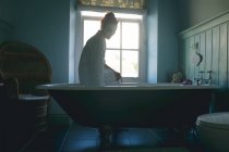Женщина сидит на ванне, проверяя воду в ванной комнате дома — стоковое фото