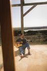 Молодой человек играет на гитаре на крыльце пляжного домика — стоковое фото