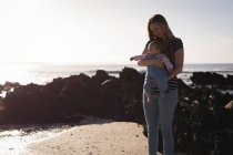 Mère avec bébé debout à la plage par une journée ensoleillée — Photo de stock