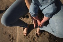 Низька частина дитини, що сидить на колінах матерів на пляжі — стокове фото
