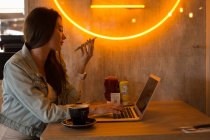 Жінка розмовляє на мобільному телефоні, використовуючи ноутбук у кафе — стокове фото