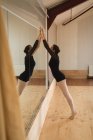 Vista lateral da bailarina que se estende na frente do espelho no estúdio — Fotografia de Stock