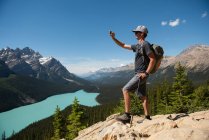 Homem clicando em fotos com telefone celular enquanto está em pé em uma rocha no campo — Fotografia de Stock