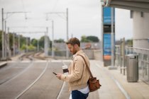 Uomo intelligente che utilizza il telefono cellulare in piattaforma alla stazione ferroviaria — Foto stock