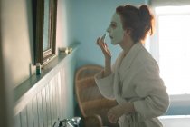 Вид збоку жінки, що застосовує маску для обличчя вдома — стокове фото